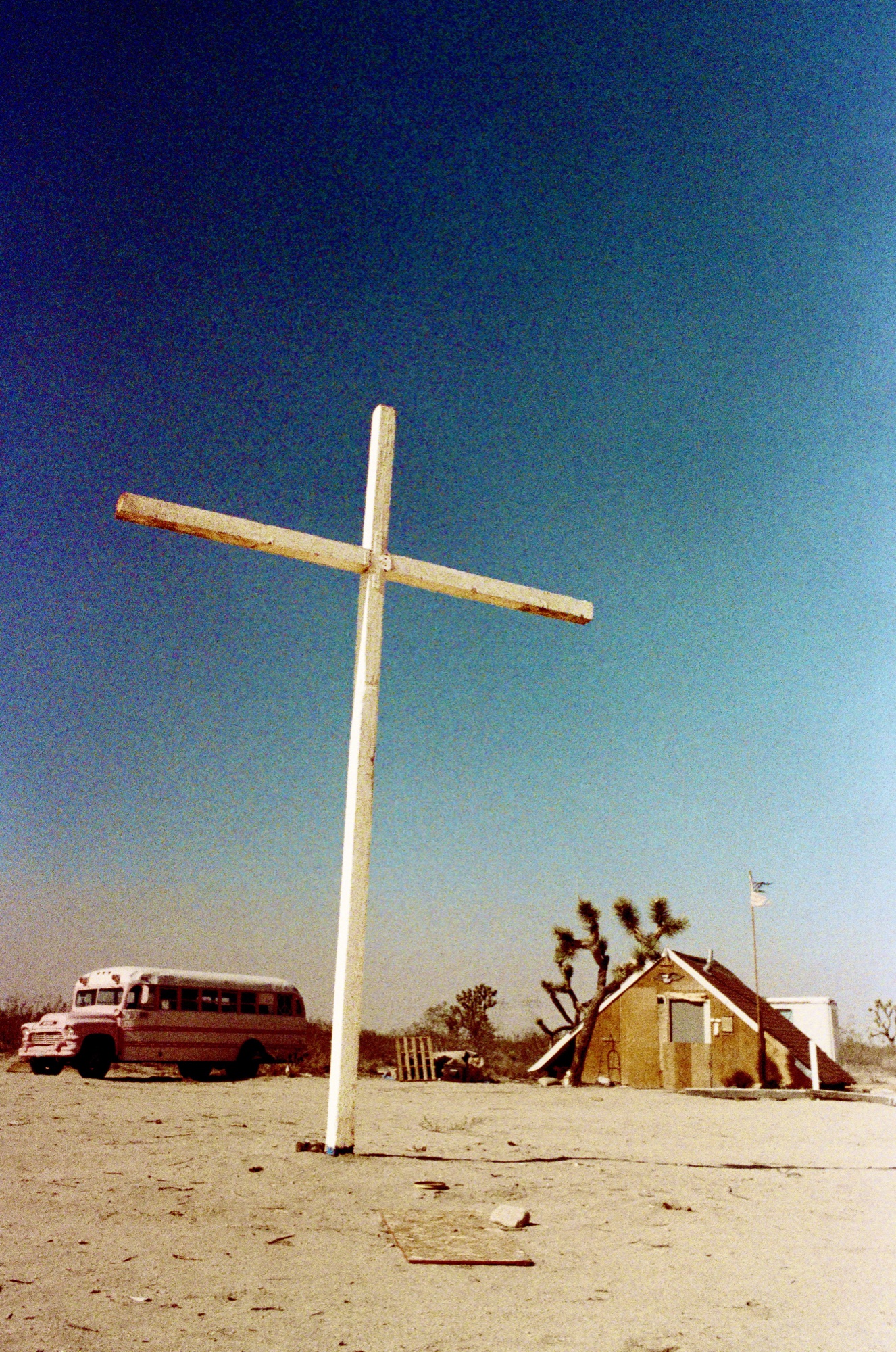 Wooden cross stands tall against a deep blue sky, Mojave landscape.