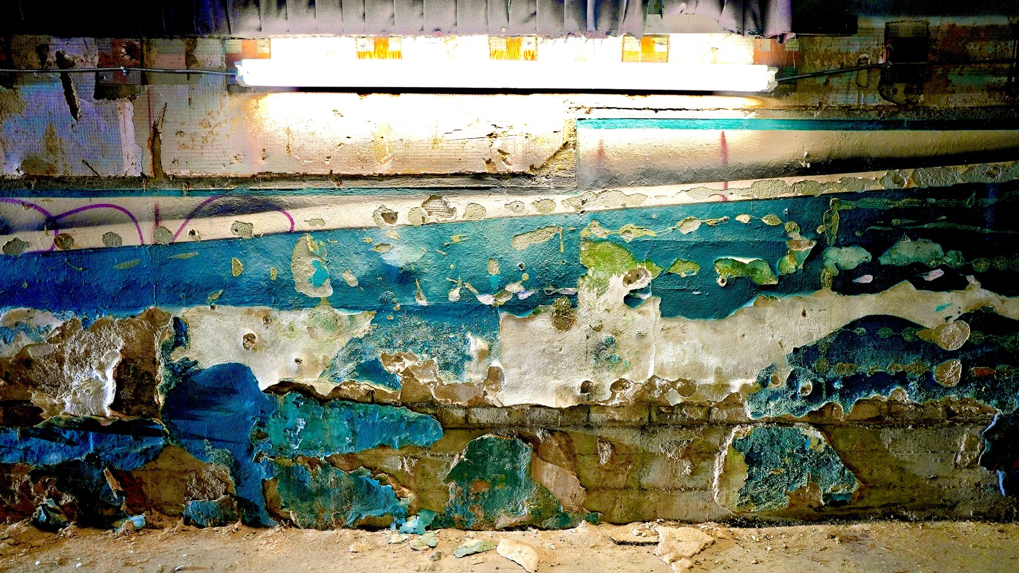 Peeling teal and cream paint on a decaying wall lit by a bare fluorescent tube — interior of the abandoned Huntridge Theater, Las Vegas.
