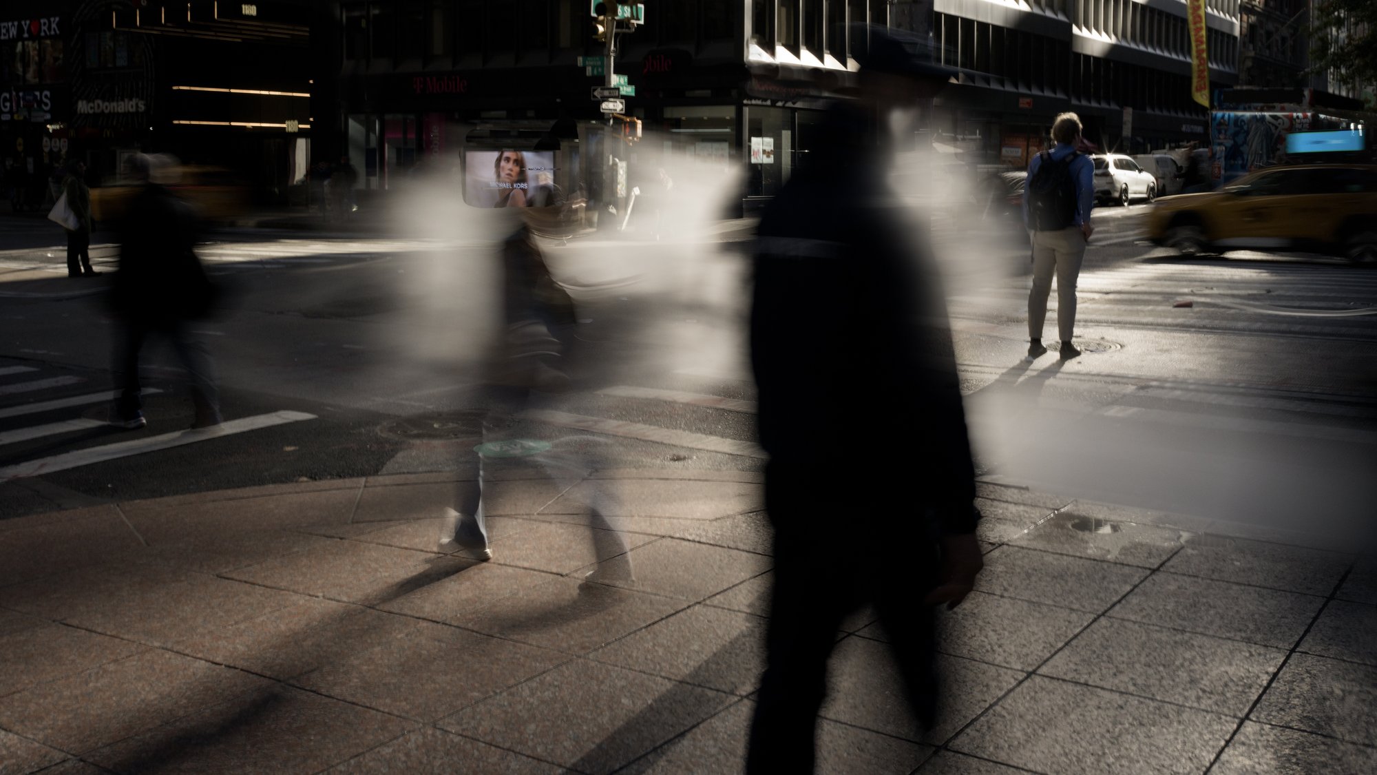 Ghosted silhouettes of pedestrians in motion at a Midtown Manhattan crosswalk, deep shadow and hard afternoon light.