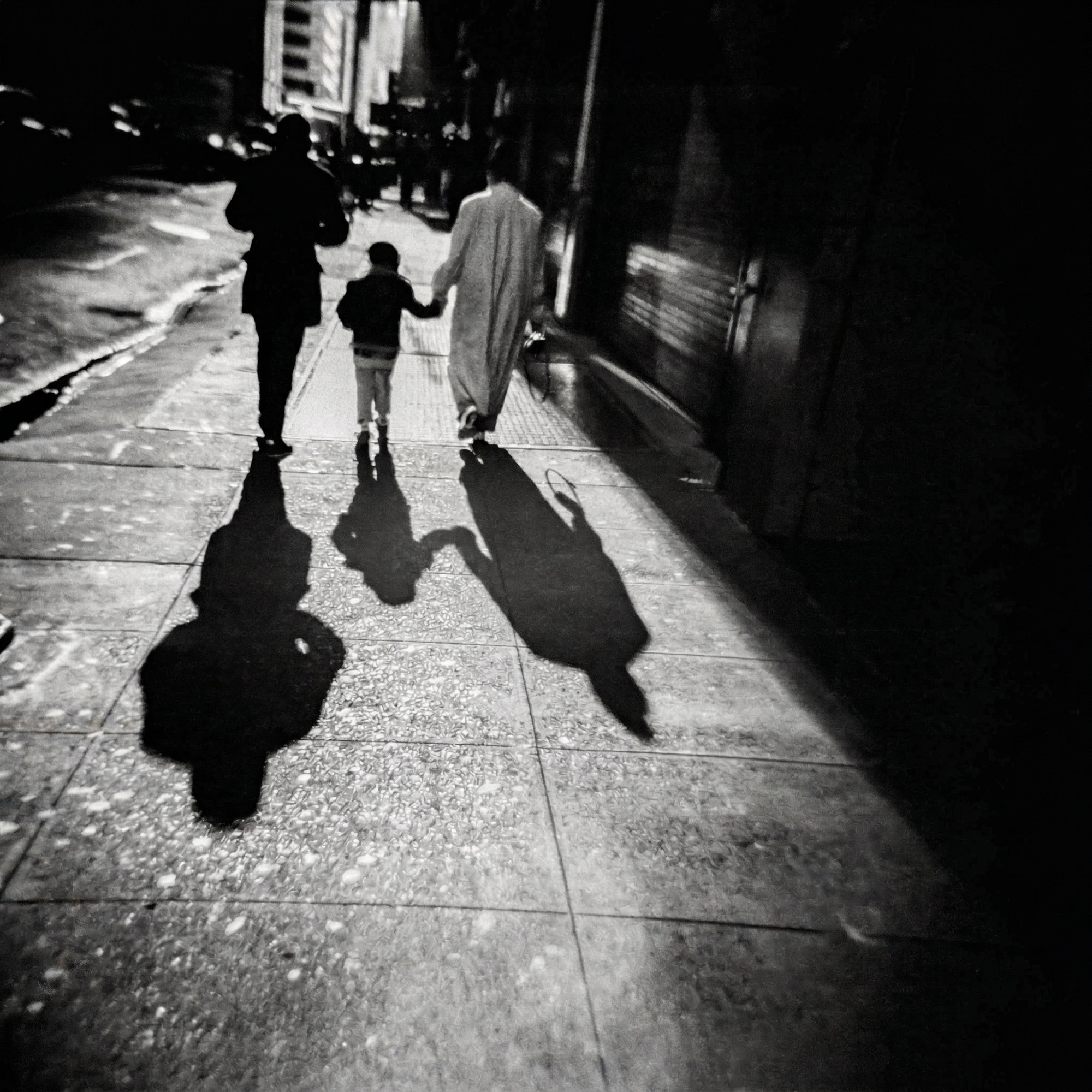 Mother, father and child cast long shadows on a city sidewalk at night.