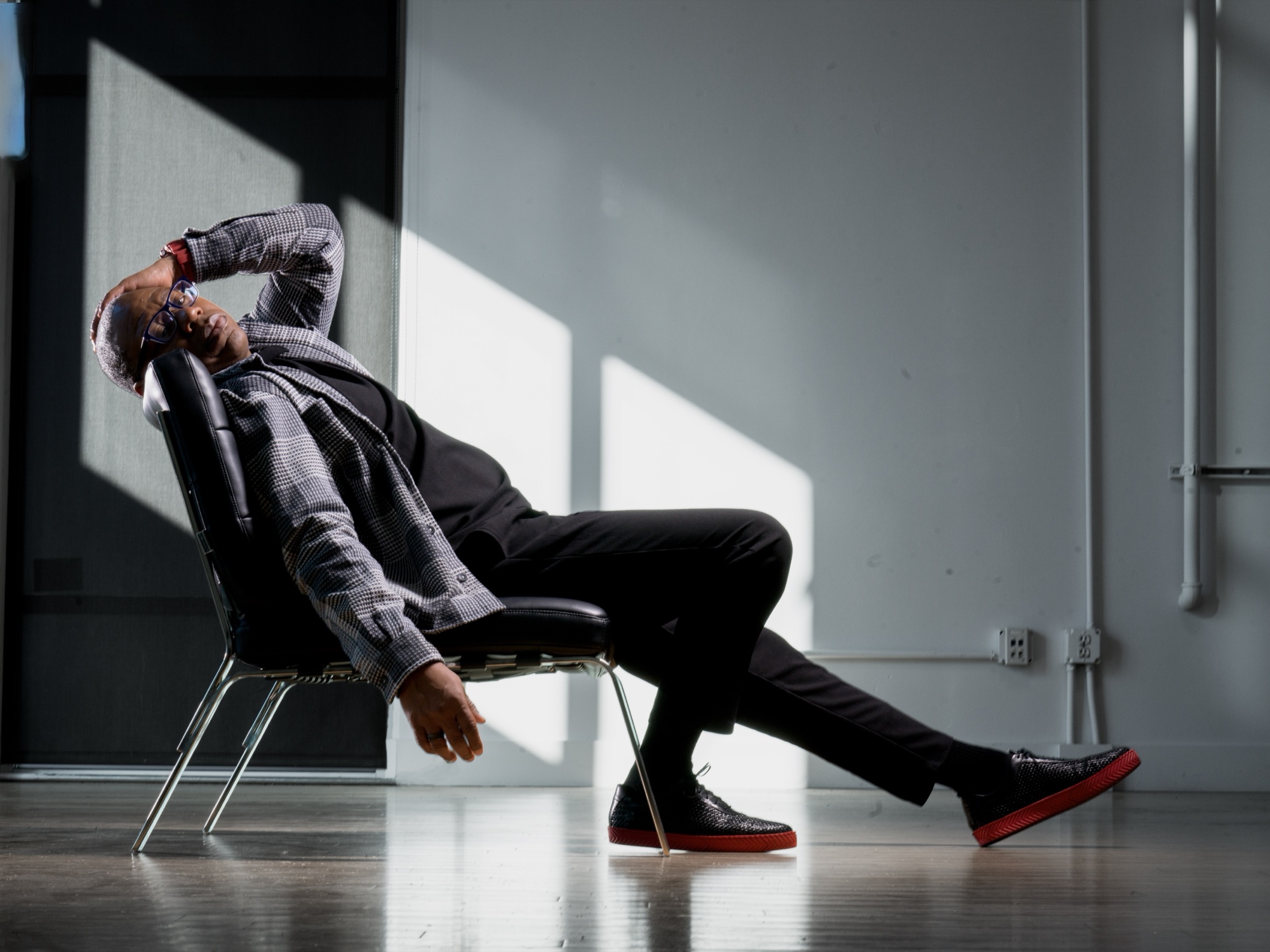 Will the Show reclining in a chair in the Post Road Loft, plaid suit, daylight.